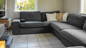 A modern living room with a grey sectional sofa, a flat-screen TV, and a window with blinds. - Holiday Home in HenÃ¥n (Henån)