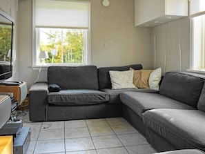 Una sala de estar moderna con un sofá seccional gris, un televisor de pantalla plana y una ventana con persianas.