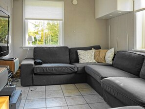 A modern living room with a grey sectional sofa, a flat-screen TV, and a window with blinds.
