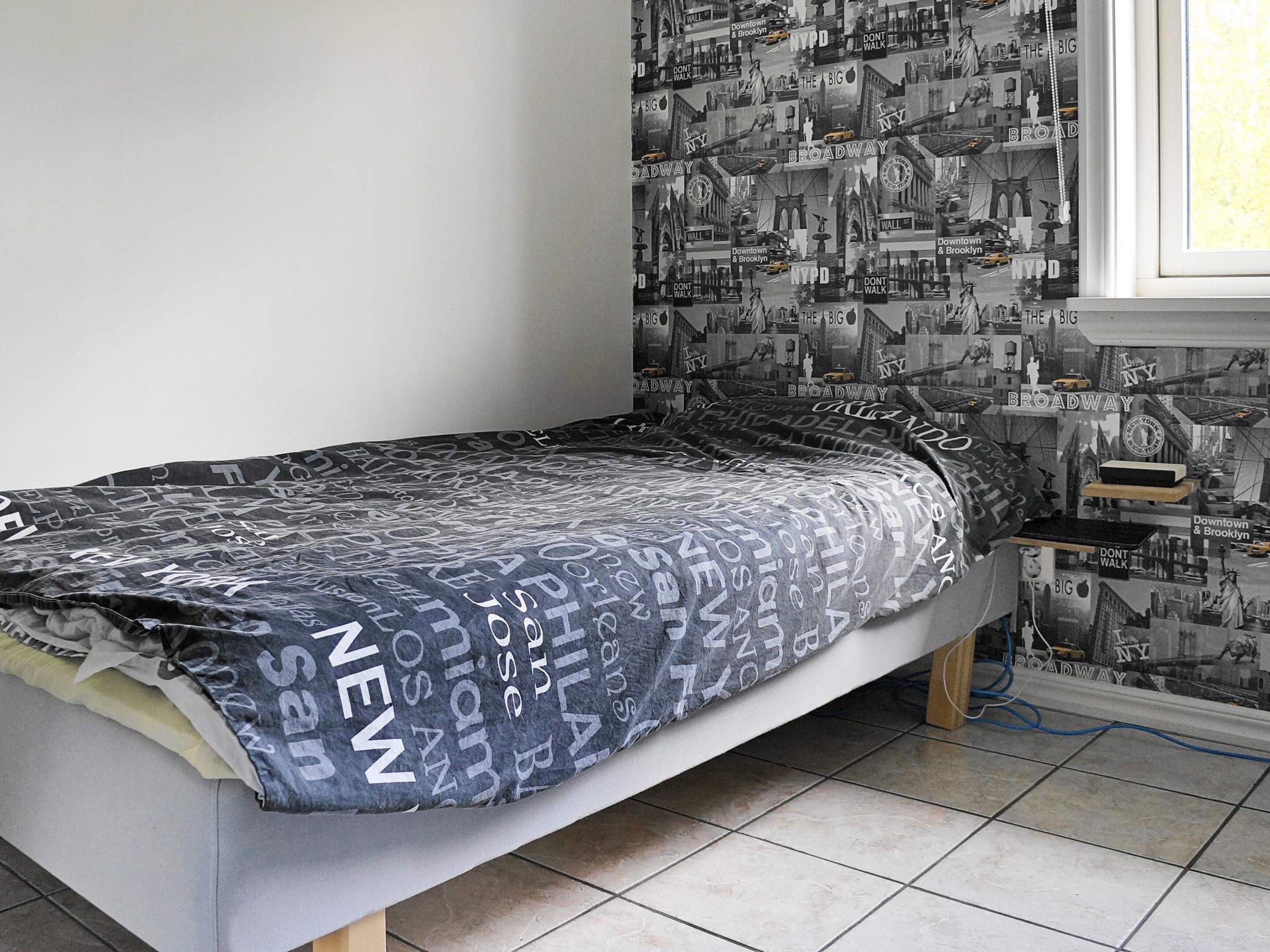 A bedroom with a bed, a window, and a wall with printed images.