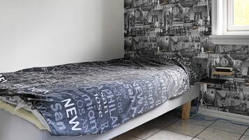 A bedroom with a bed, a window, and a wall with printed images.