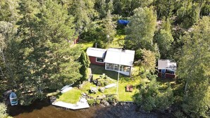 Une maison entourée d’une forêt dense, avec une jetée qui s’avance sur une étendue d’eau.