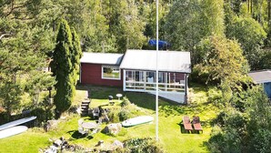 Un chalet au bord du lac, doté d’un porche vitré, entouré d’une pelouse et d’un petit quai.