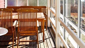 Une terrasse en bois avec une table et des chaises, de grandes fenêtres et une plante en suspension.