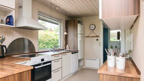 A modern kitchen with wooden cabinets, a built-in oven, a sink, and a window with a view of greenery. - Simplistic Holiday Home in Blokhus With Sea Nearby (Aabenraa)