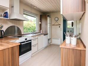 A modern kitchen with wooden cabinets, a built-in oven, a sink, and a window with a view of greenery. - Simplistic Holiday Home in Blokhus With Sea Nearby (Aabenraa)