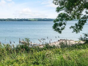 A lakeside view with a dock, grassy banks, and distant hills.