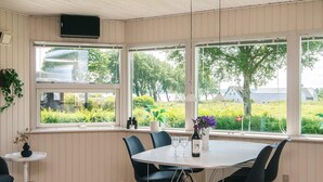 A dining area with a round table, black chairs, a small side table, and a window with a view of greenery and buildings. - Simplistic Holiday Home in Blokhus With Sea Nearby (Aabenraa)
