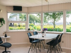 A dining area with a round table, black chairs, a small side table, and a window with a view of greenery and buildings. - Simplistic Holiday Home in Blokhus With Sea Nearby (Aabenraa)
