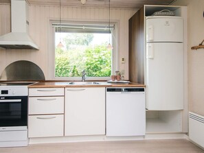 A kitchen with white cabinetry, a built-in oven, a dishwasher, and a window with a view of greenery.