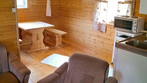 L’intérieur d’un chalet accueillant, avec des murs en bois, une table en bois, un banc, un canapé, un coin cuisine équipé d’un grille-pain et une fenêtre avec des rideaux.