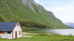 Un petit bâtiment blanc, coiffé d’un toit rouge, situé près d’un lac et entouré de collines et de montagnes verdoyantes.