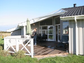 Ein überdachter Außenbereich mit einer Holzterrasse, einem Tisch, Stühlen und einem grünen Sonnenschirm.