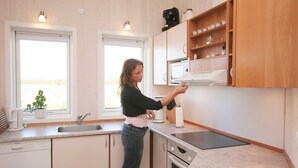 A kitchen with white cabinets, a countertop, a sink, a stove, and a window with a plant on the windowsill.