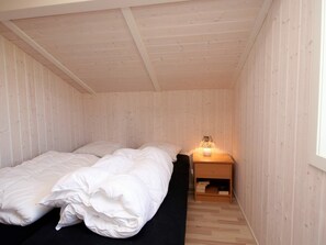Una cama individual con ropa de cama blanca en una habitación con paredes de madera y techo inclinado.