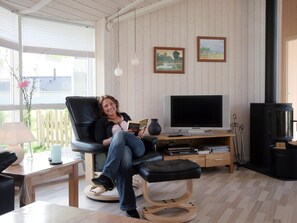 A cozy living room with a black leather chair, a flat-screen TV, a wooden table, and a black fireplace. - 4 Star Holiday Home in Rude (Bisserup)