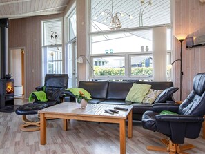 A modern living room with a fireplace, leather sofas, a coffee table, and large windows offering a view of the outdoors. - 4 Star Holiday Home in Rude (Bisserup)
