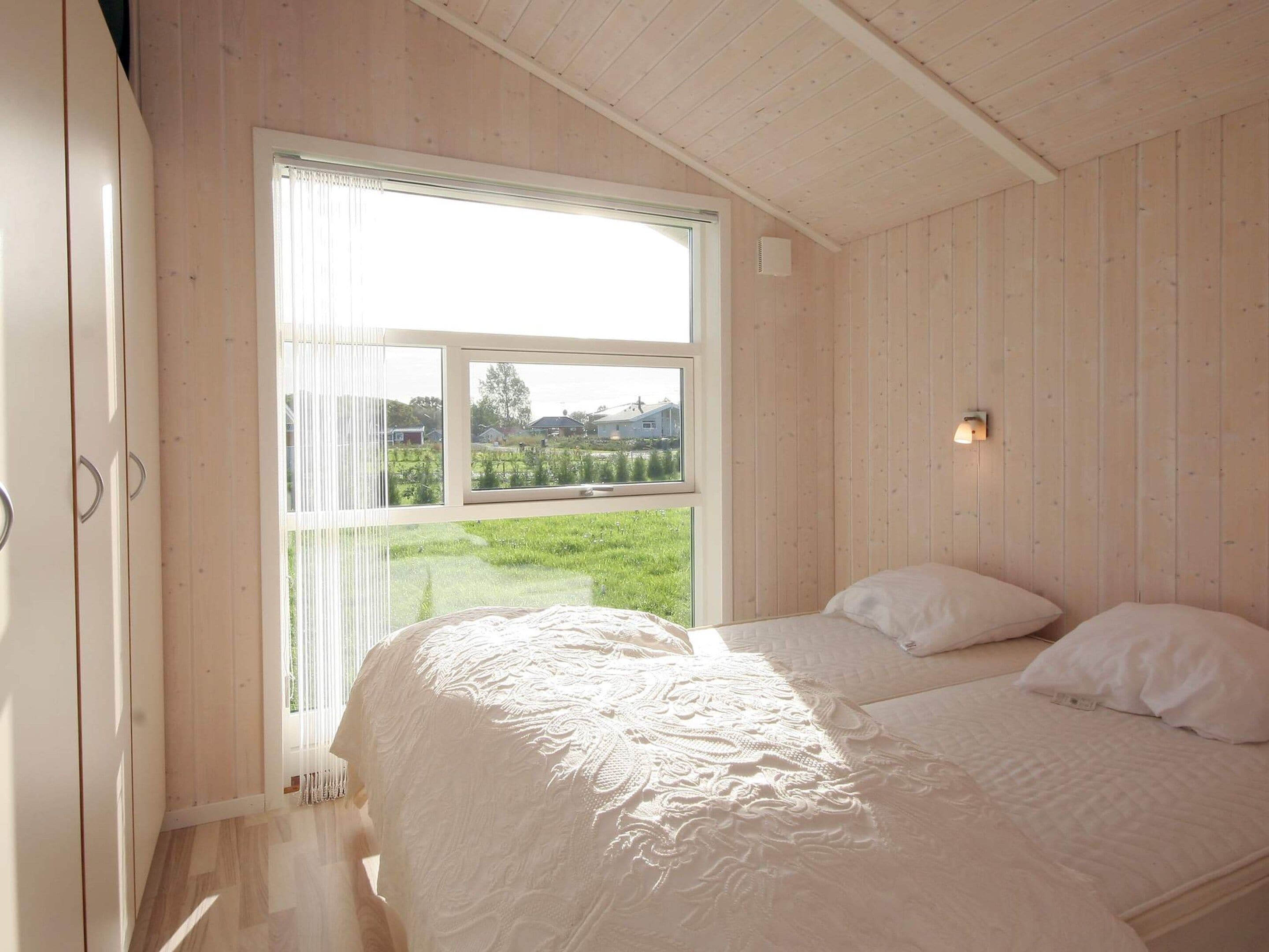A bedroom with a large window, a bed with white bedding, and wooden paneling on the walls.