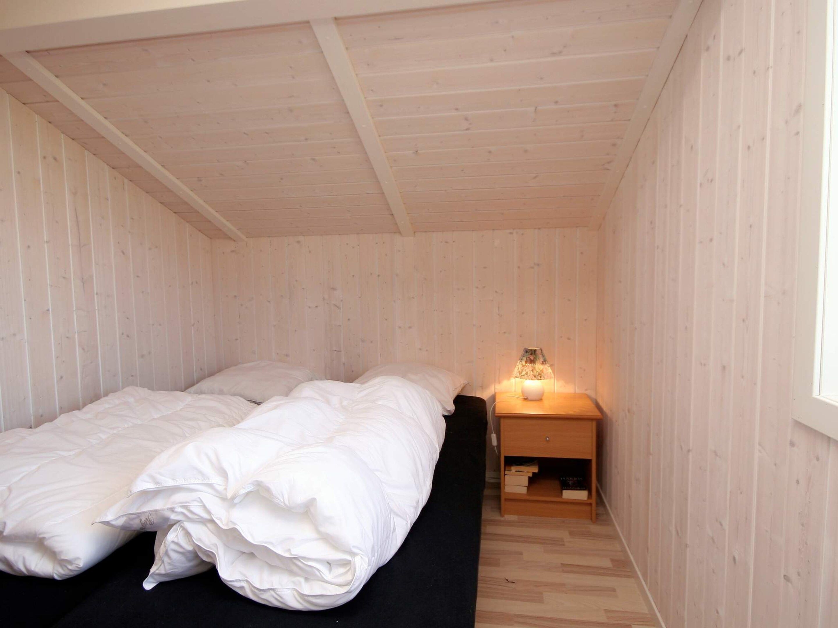 A single bed with white bedding in a room with wooden walls and a sloped ceiling.