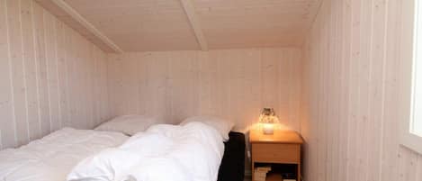 A single bed with white bedding in a room with wooden walls and a sloped ceiling.