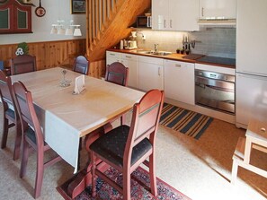 Uma sala de jantar com mesa e cadeiras, uma cozinha com eletrodomésticos modernos e uma escada de madeira.