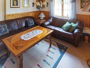 Uma sala de estar com um sofá de couro marrom, uma mesa de centro de madeira e um tapete estampado.