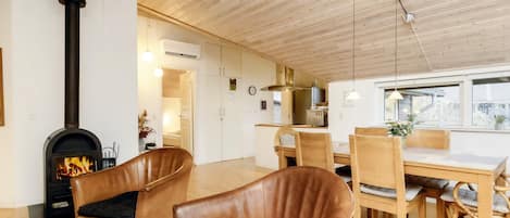 A cozy interior with a fireplace, leather chairs, a dining table, and a kitchen area.