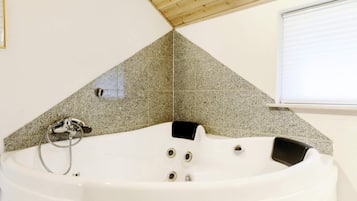 Un baño moderno con una bañera independiente, techo de madera y ventana con persianas.