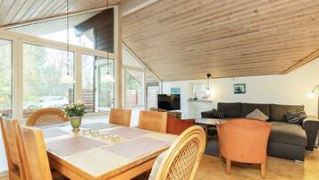 A spacious loft with a high ceiling, a dining area with a table and chairs, a sofa, and a television.