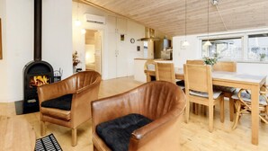 A cozy interior with a fireplace, leather chairs, a dining table, and a kitchen area.