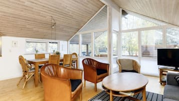 A spacious living area with a wooden ceiling, large windows, and a television.
