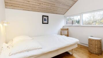 Une chambre avec un plafond en bois, un lit avec une literie blanche, une petite chaise, une fenêtre et un panier en osier.