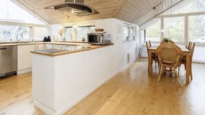 A modern kitchen with a central island, wooden ceiling, and large windows.