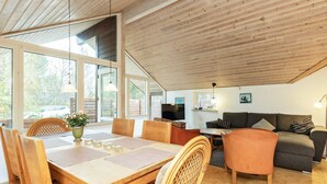 A spacious loft with a high ceiling, a dining area with a table and chairs, a sofa, and a television.