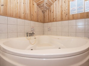 A bathroom with a large bathtub, wooden panel walls, and tiled flooring. - 4 Star Holiday Home in Skjern (Skjern)