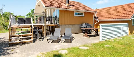 Una casa de dos pisos con un patio, mobiliario exterior y una zona de barbacoa.