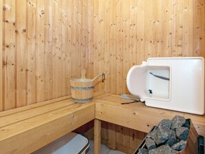 Un sauna con paredes de madera, un banco de madera, una pila de piedra y una tina de sauna blanca.