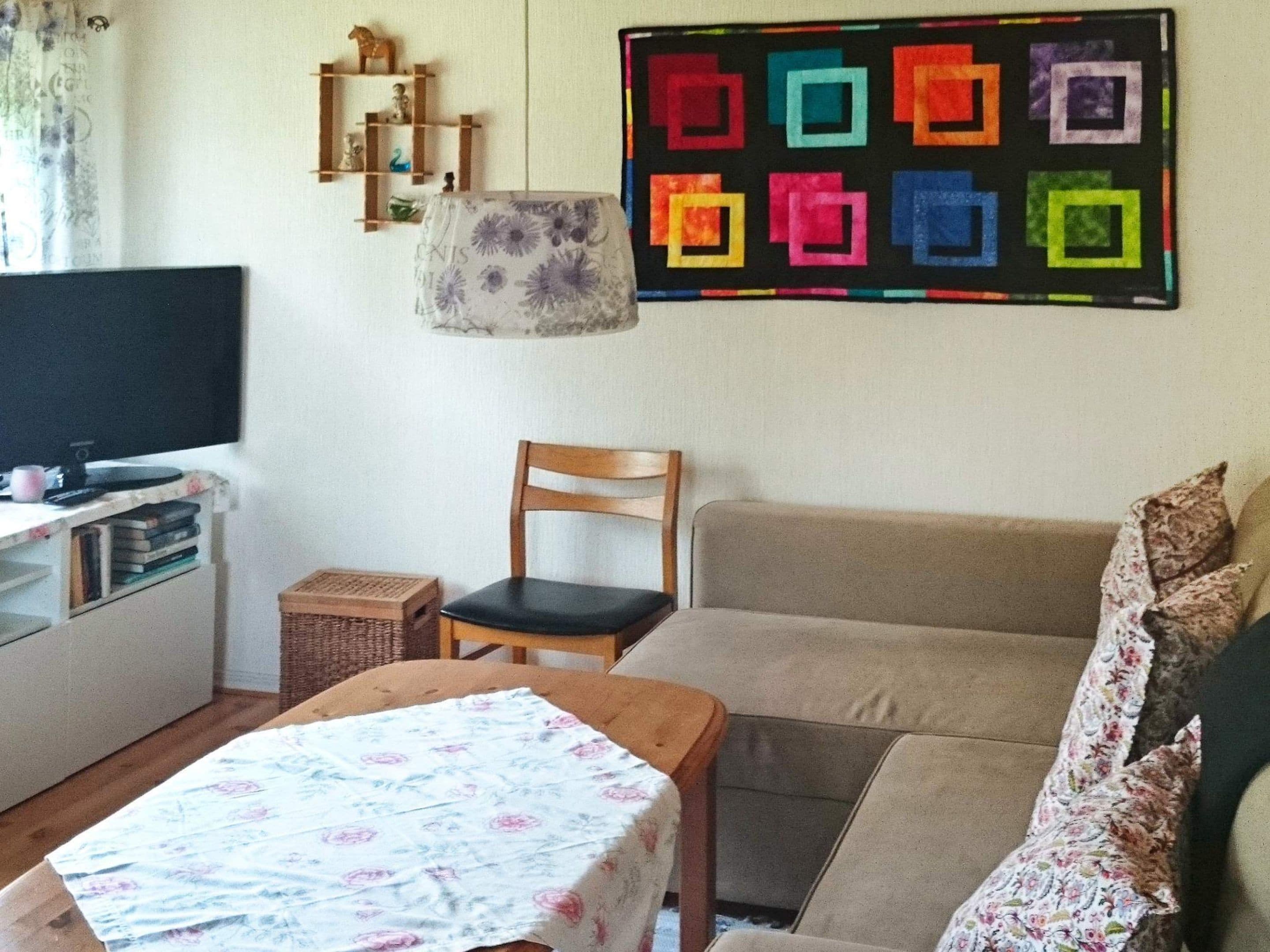 A living room with a television, a sofa, a chair, and a table with a floral tablecloth.