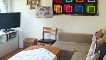 A living room with a television, a sofa, a chair, and a table with a floral tablecloth.