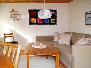 A cozy living room with a wooden table, a sofa, and a colorful quilt hanging on the wall. - 4 Person Holiday Home in Bello (Hjältevad)