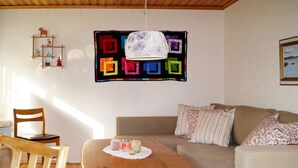 A cozy living room with a wooden coffee table, a beige sofa, and a colorful quilt hanging on the wall. - 4 Person Holiday Home in Bello (Hjältevad)