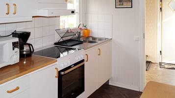 A modern kitchen with white cabinetry, a stove, a microwave, and a coffee maker.