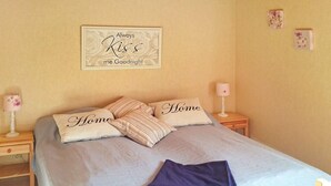A neatly made bed with a light-colored bedspread and pillows, a bedside table with a lamp, and a wall-mounted sign with a floral design. - 4 Person Holiday Home in Bello (Hjältevad)