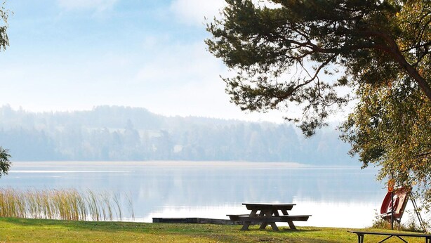 A picnic table and bench by a calm lake with a forest in the background. - 4 Person Holiday Home in Bello (Hjältevad)