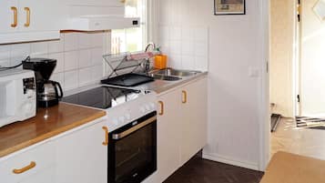 A modern kitchen with white cabinetry, a stove, a microwave, and a coffee maker.