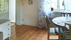 A room with a wooden floor, a white dresser, a dining table with chairs, and a window with a floral curtain. - 4 Person Holiday Home in Bello (Hjältevad)