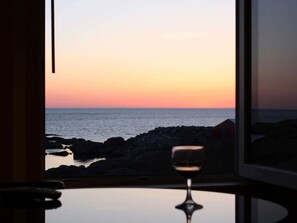 A window with a view of the sea at sunset, a glass of wine on a table, and a chair. - Holiday Home in SirevÃ¥g (Ha)