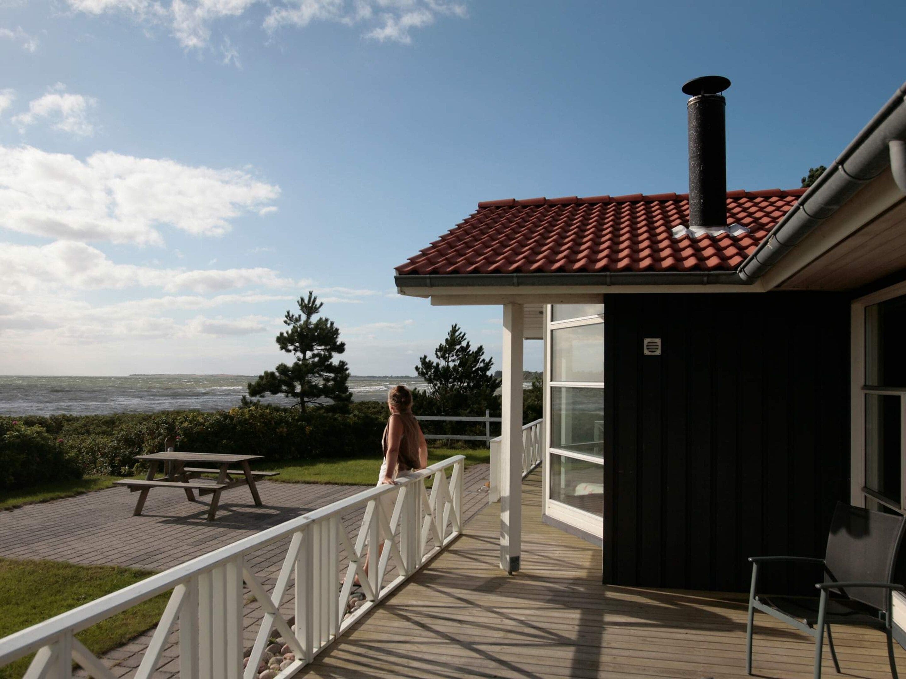 A deck with a view of the sea, a picnic table, and a small building with a chimney.