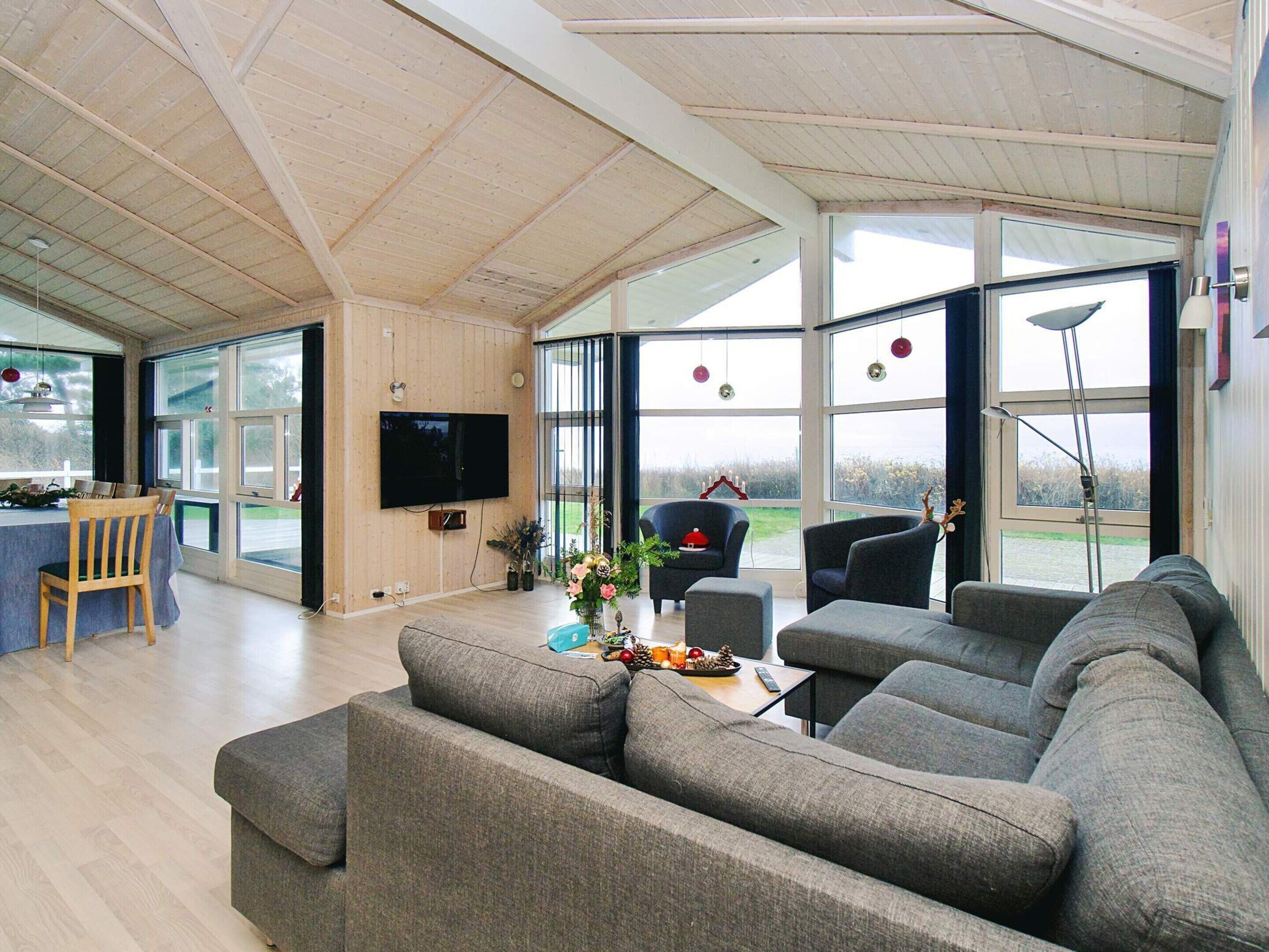 A spacious living room with a large grey sectional sofa, a television mounted on the wall, and a dining area with a table and chairs.