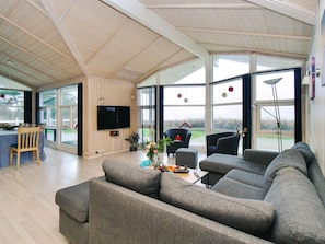 A spacious living room with a large grey sectional sofa, a television mounted on the wall, and a dining area with a table and chairs. - 5 Star Holiday Home in Gorlev (Gørlev)